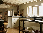 Schöne Landhausküche und ein schlichter Küchentisch unter einer weissen Holzbalkendecke