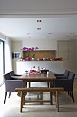 Esstisch im offenen Wohnraum mit antiker Sitzbank, modernen Sesseln und mit Blick auf die dekorierte Küchentheke
