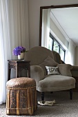 Gemütlicher Sessel vor großem, gerahmten Wandspiegel in Zimmerecke mit antikem Blumensockel, Hortensienstrauss in einer Vase und einem asiatischen Hocker