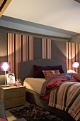 Beleuchteter Schlafraum mit Bett, Nachttischlampen, gestreifter Wandtapete & farblich passender gestreifter Tagesdecke