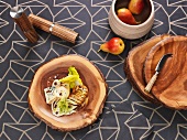 Holzbrettchen teils mit Essen dekoriert auf einer grauen gemusterten Tischdecke