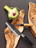 Half an artichoke and a knife on a wooden board