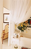 Badezimmer mit Badewanne, Beistelltischchen, Blumenstrauss & weißem Vorhang