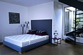 Zimmer mit blauem Doppelbett, Matratze, Dekokissen, Stehlampe & Wohnungstreppe