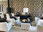 Wohnzimmer mit gemusterter Wandtapete, weissen Sesseln & Kaminofen