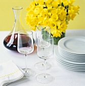 Red wine, glasses, pile of plates, vase of daffodils