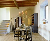 Ländlicher Wohnraum mit Balkendecke, gedecktem Tisch, hängendem Kerzenleuchter & Treppenaufgang aus Stein