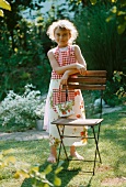A girl wearing and apron and carring a bag with a strawberry pattern in a garden