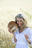 Blonde Frau mit Brotlaib im Getreidefeld