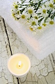 Burning candle and towel with white asters