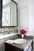 Eleganter Waschtisch mit rotem Blumensträusschen unter derbem Badezimmerspiegel mit geschweisstem Metallrahmen