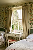 Typisch englisches Landhaus-Schlafzimmer mit floraler Tapete, kleinem Schreibtisch und zwei gemachten Betten