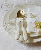 A white place setting with an embroidered serviette and a flower