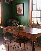 Antiker Esstisch mit filigranen Metallstühlen in Essraum mit dunkelgrünen Wänden und Bodenfliesen