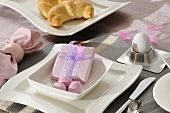 A breakfast place setting with a wrapped present and pink Easter decoration