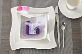 A present wrapped in purple with a ribbon and a feather in a bowl