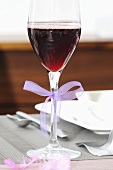 A glass filled with a red drink and decorated with a bow