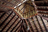 An Indian wooden ceiling with an offset roof and a hanging metal pot