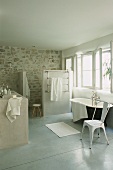 Grosszügiges Badezimmer mit Natursteinwand, freistehender Badewanne, gemauertem Waschtisch & Dusche hinter Trennwand