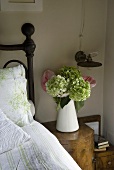 Flowers in a white pitcher on a bedside table