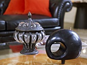 Antique container made of metal and glass and wooden sculpture in front of a sofa