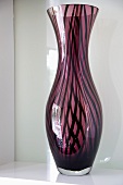A purple striped vase in front of a white glass panel