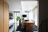 A view into a dining room with a wooden table, designer chairs and shiny black floor tiles