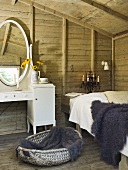 A rustic room with wooden walls - a fur on the bed and a white dressing table
