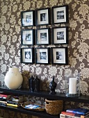 A black shelf and black-framed pictures on a wall hung with floral wallpaper