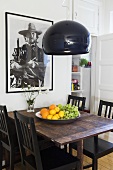 A fruit bowl on a dark wooden dining table with a black lampshade hanging above it