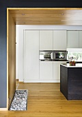 A view into an open-plan kitchen with a wooden wall and ceiling and a white fitted cupboard