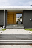An entrance way to a grey, newly-built house with concrete steps and a wooden doorway