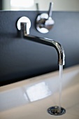 A designer wall tap on a black wall with running water