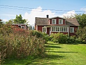 A garden with a red-painted wooden houser and white windows