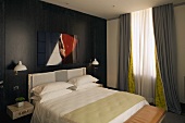 Schlafraum mit Doppelbett vor schwarzvertäfelter Holzwand und bodenlangen grauen Vorhängen am Fenster