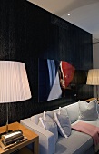 Light gray sofa in front of a wall with black paneling with table lamps and pleated shades