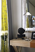Delicate stainless steel table lamp on a wooden table in front of a wall mirror