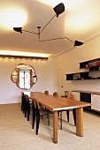 Black ceiling lamp with movable cantilever arms above a long wooden table and chairs in 50's style