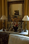 Table lamps on the top of a marble table and a mirror with a gold frame