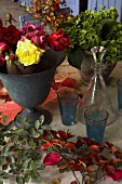 An arrangement of roses in an antique metal vase, flower pot and a decanter
