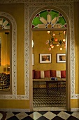 Blick durch Rundbogen in marokkanisches Wohnzimmer mit Bordüren an gelben Wänden und gemustertem Fliesenboden