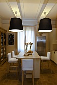 Dining room with black lampshades hanging from the ceiling and a kitchen counter with bar stools