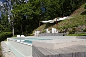 A pool in the garden and an awning above a wooden deck on a slope