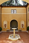 A fountain in the courtyard of a Mediterranean villa with a terracotta floor and a yellow facade