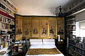 Bedroom with a double bed in front of an Asian screen and floor to ceiling bookshelves