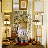 A collection of pictures in gold frames in front of a mirror with various containers on the shelf