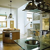 An open-plan kitchen with a stainless steel sink set into a glass work surface and a round island counter