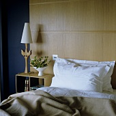 Bed in front of a wood paneled wall and night stand with table lamp