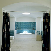 A bathroom with a vaulted ceiling - a view through an open curtain onto a bath in a niche with blue wall tiles