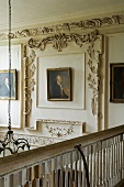 A view from a gallery onto oil paintings on a wood panelled wall with carvings